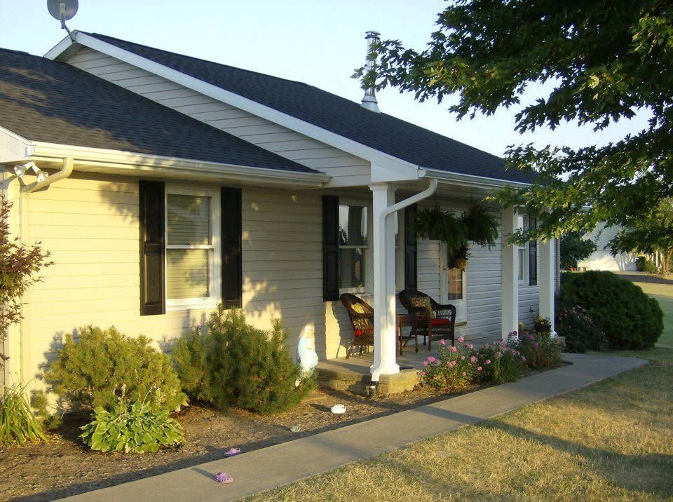 Suburban house with yellow siding, front porch, and landscaped yard in daylight.
