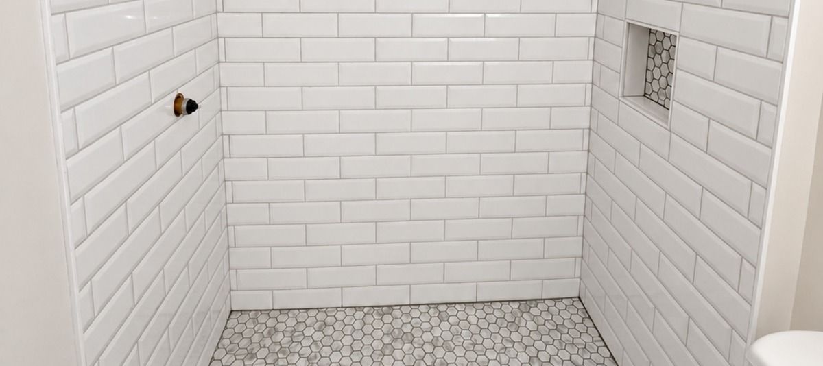 Empty white-tiled shower stall with pebble floor and wall fixtures