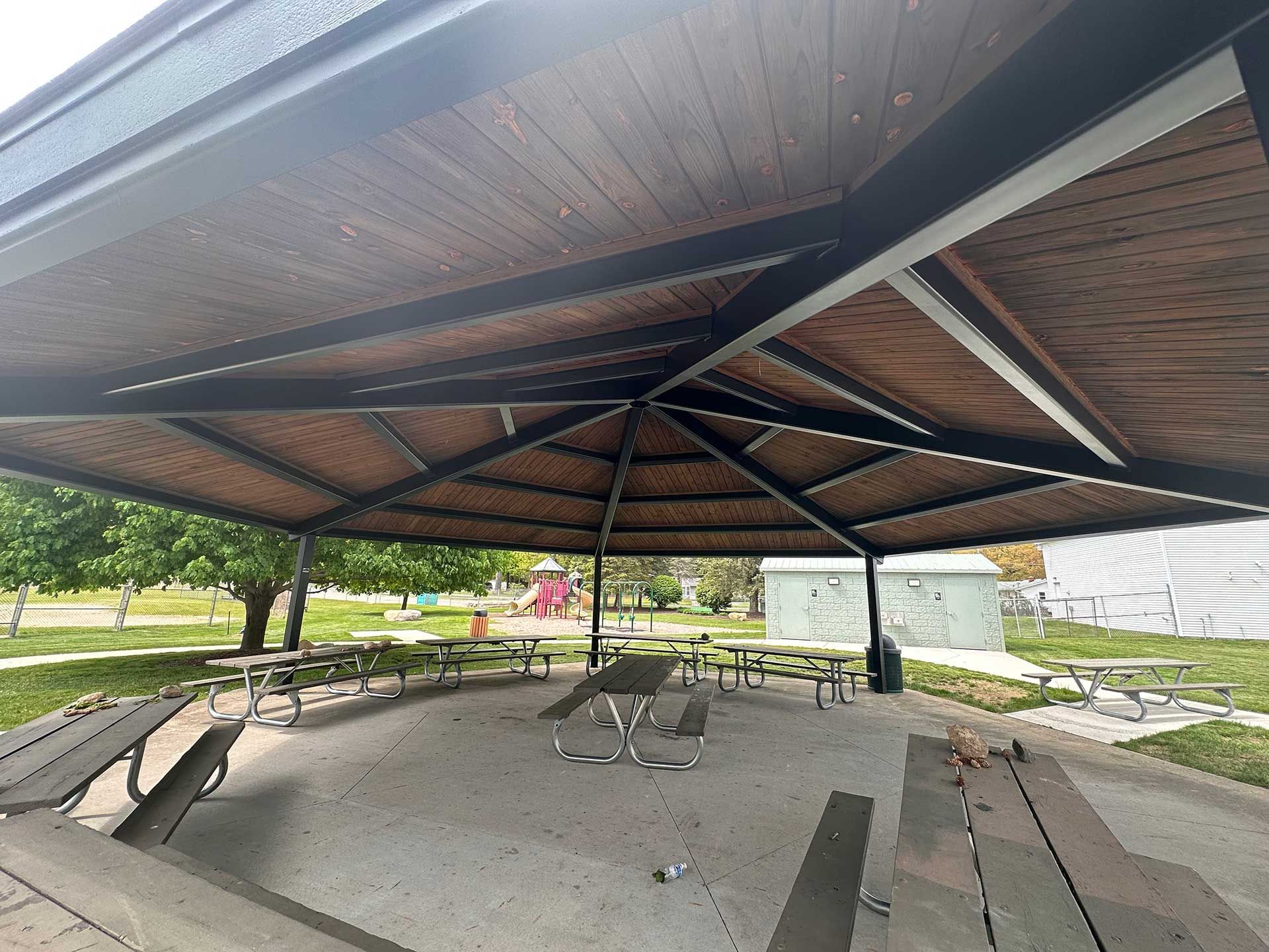 a covered picnic area with tables and benches in a park
