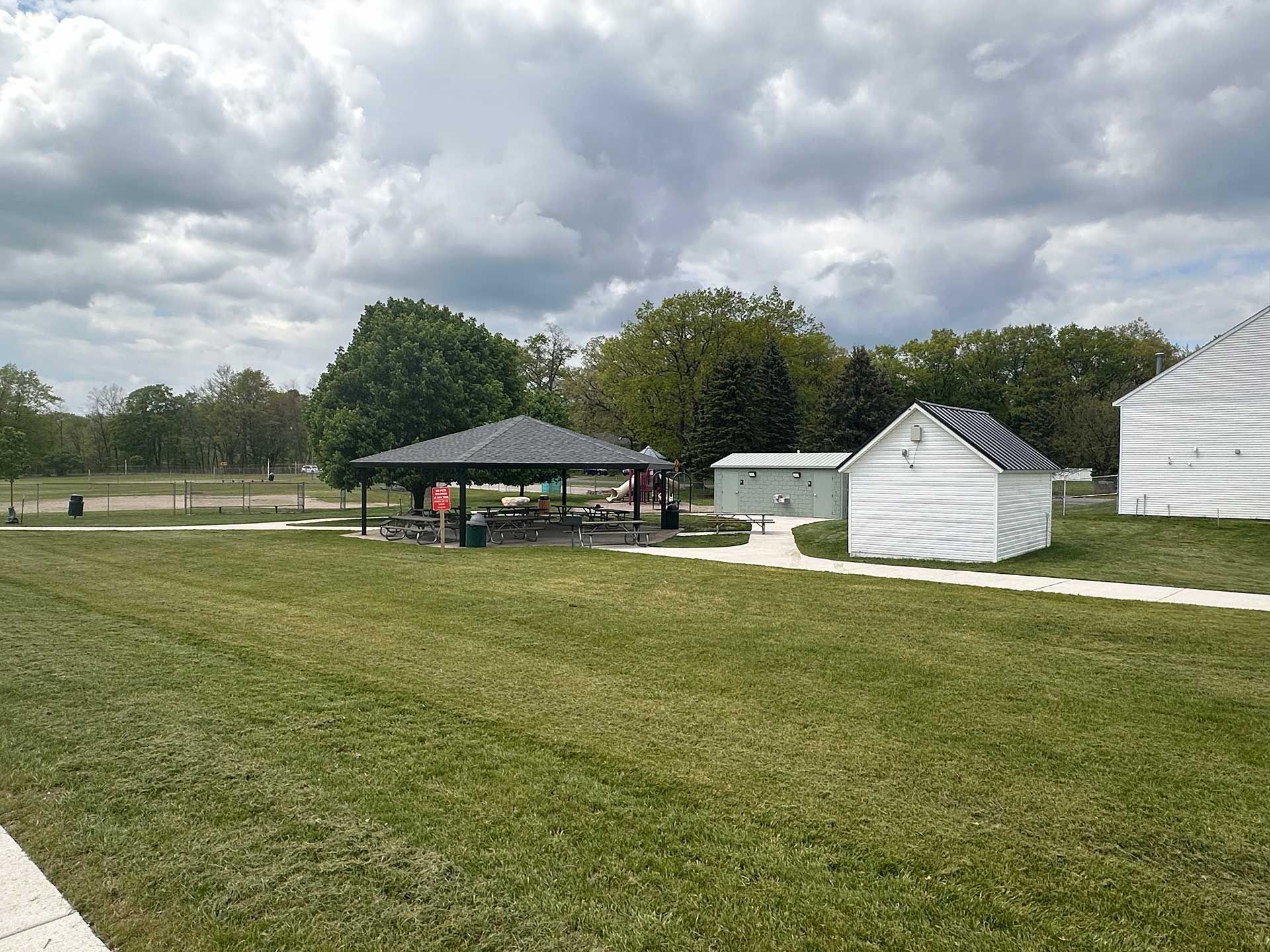 a large grassy field with a pavilion and sheds in the background