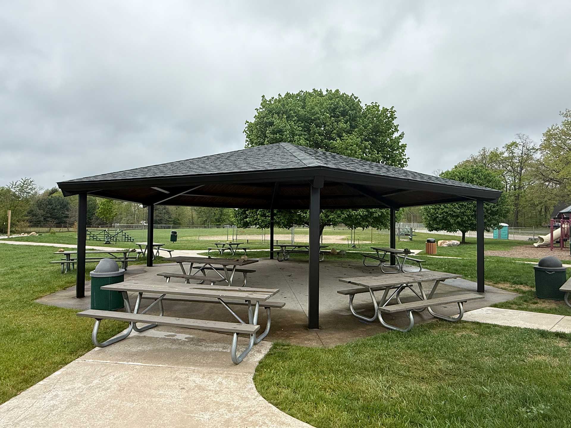 a picnic shelter with tables and benches in a park on a cloudy day
