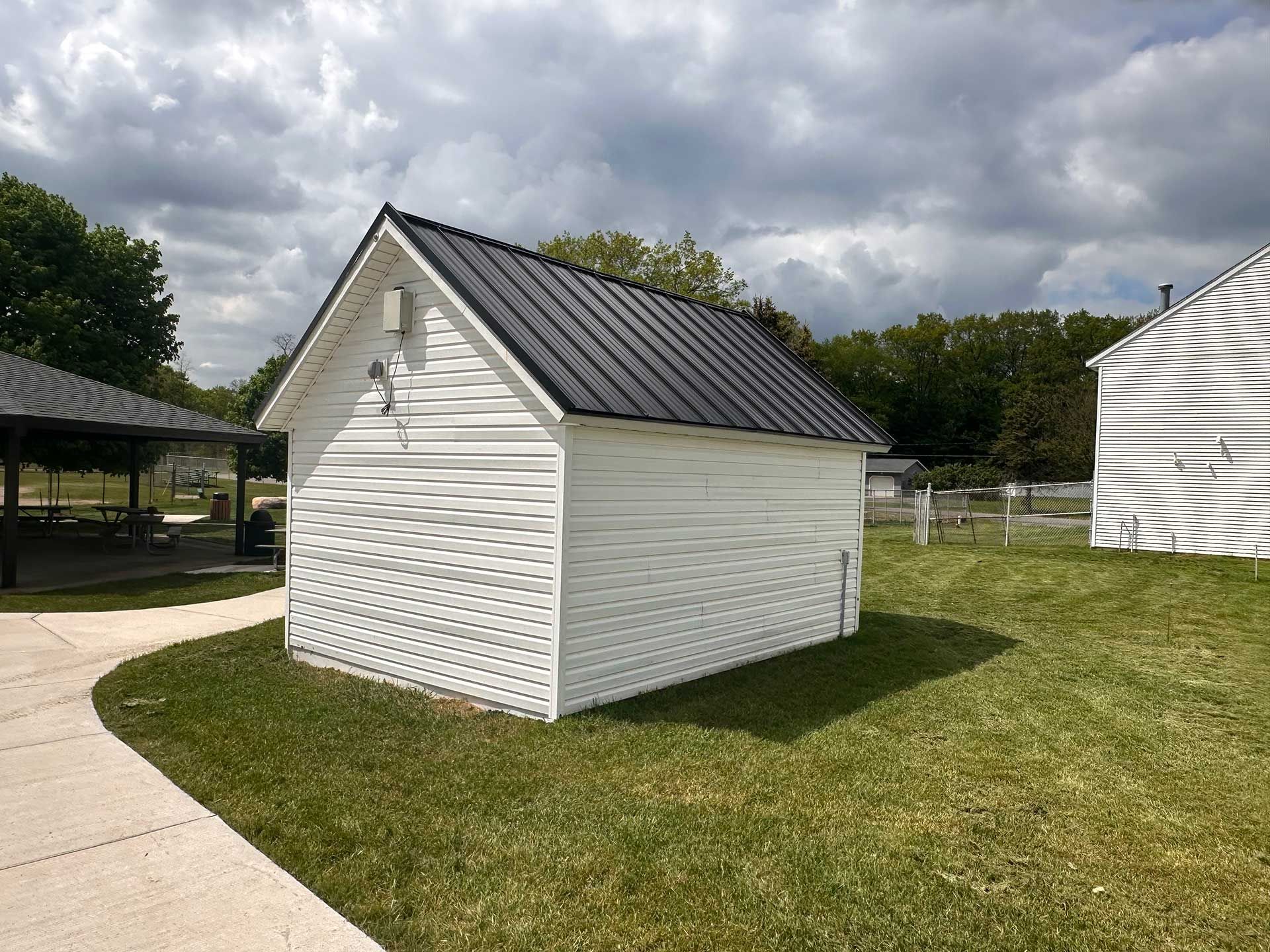 a small white shed with a black roof is sitting in the grass