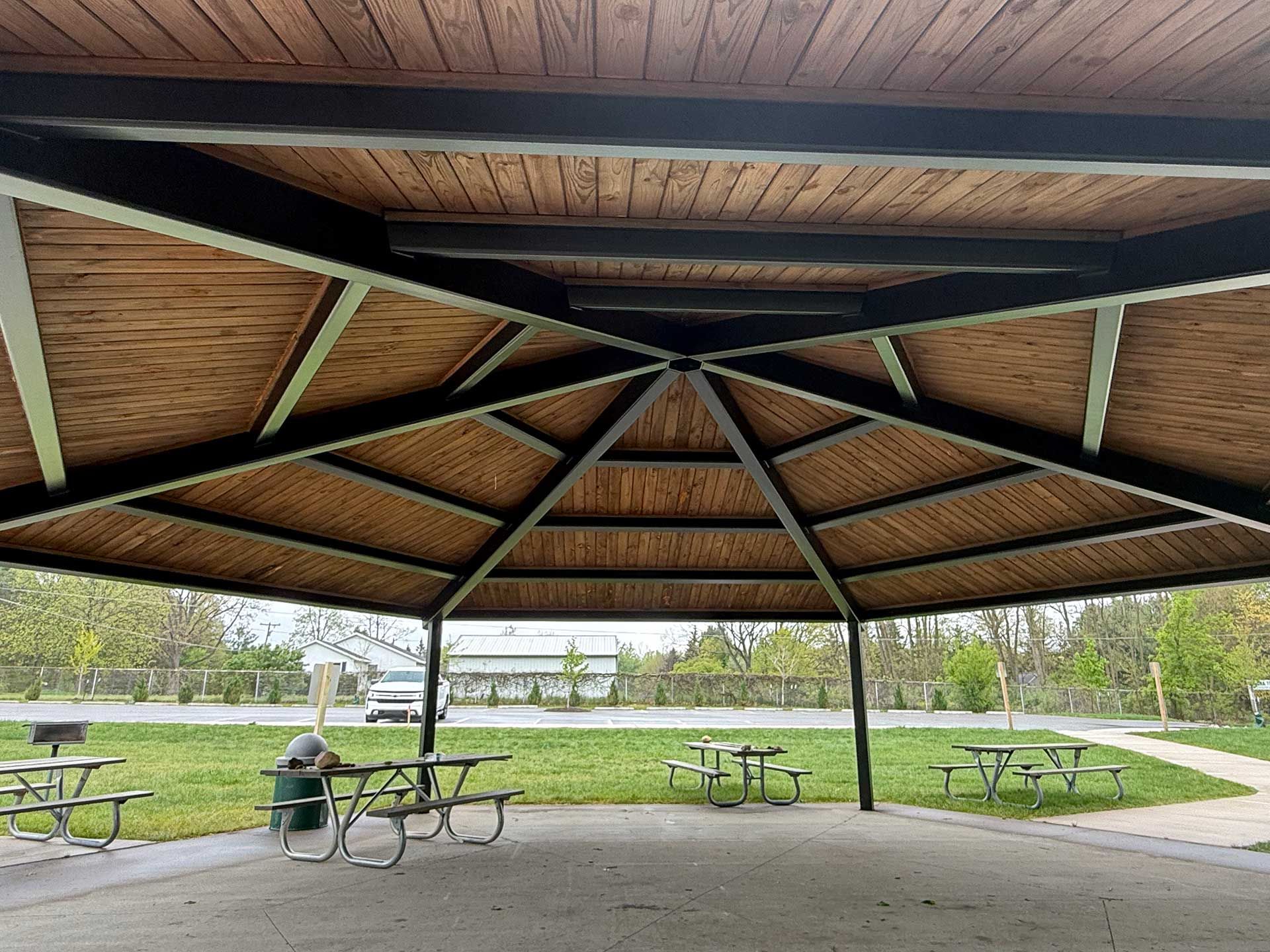 a wooden gazebo with picnic tables underneath it in a park