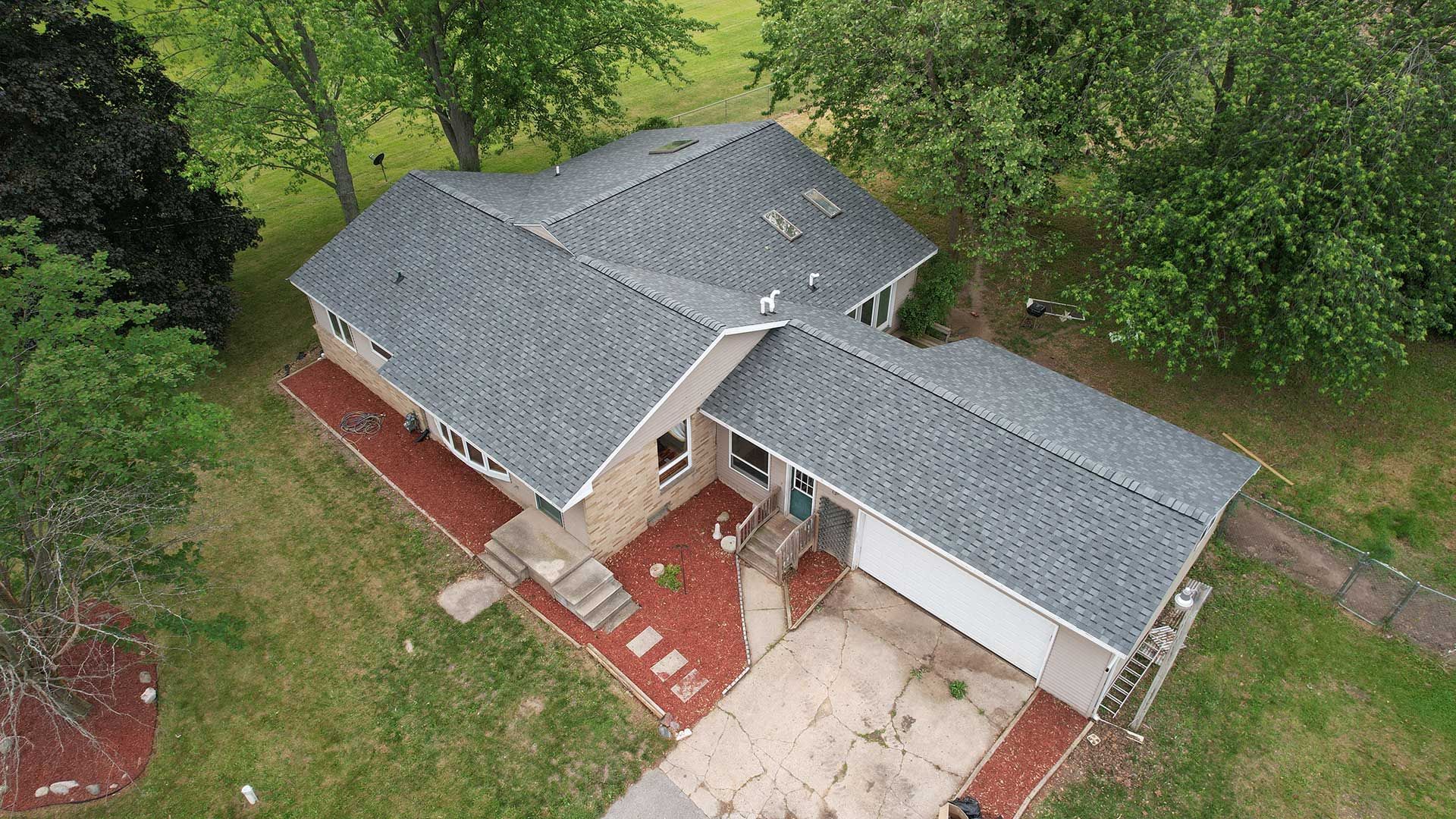 an aerial view of a house with a new roof surrounded by trees