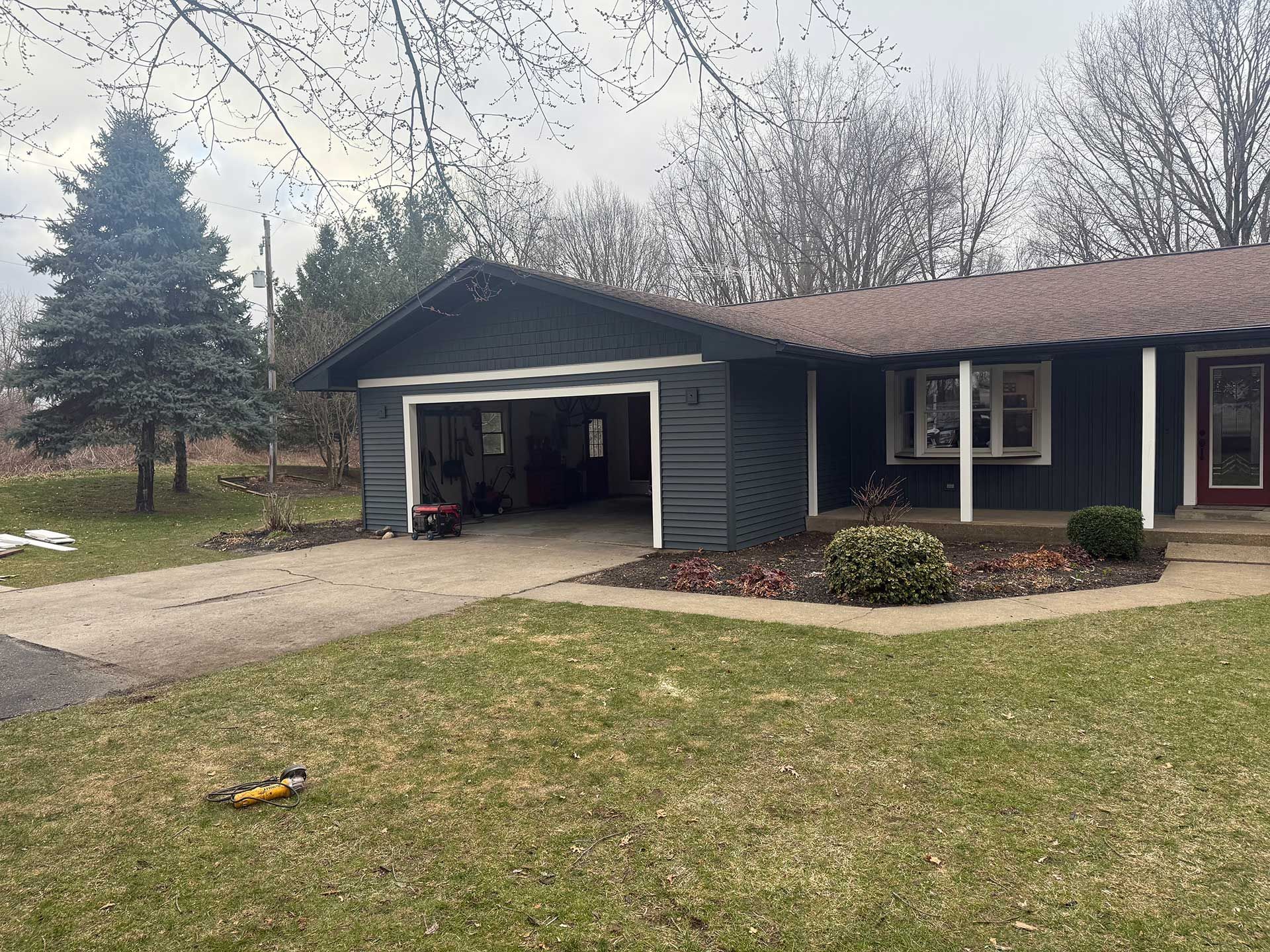 a house with a garage and a porch is sitting on top of a lush green field