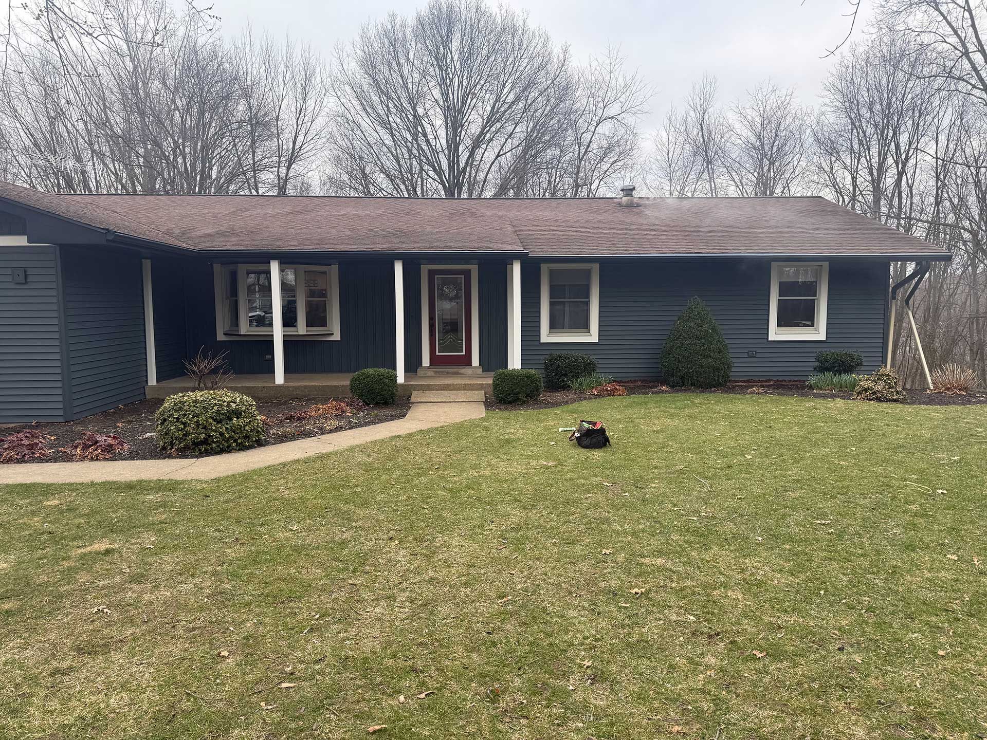 A blue house with a brown roof and a large lawn in front of it