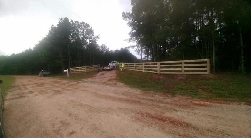 A dirt road with a wooden fence on the side of it.