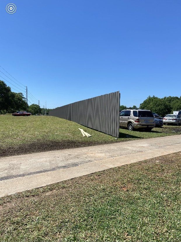 A long wooden fence surrounds a parking lot with cars parked behind it.