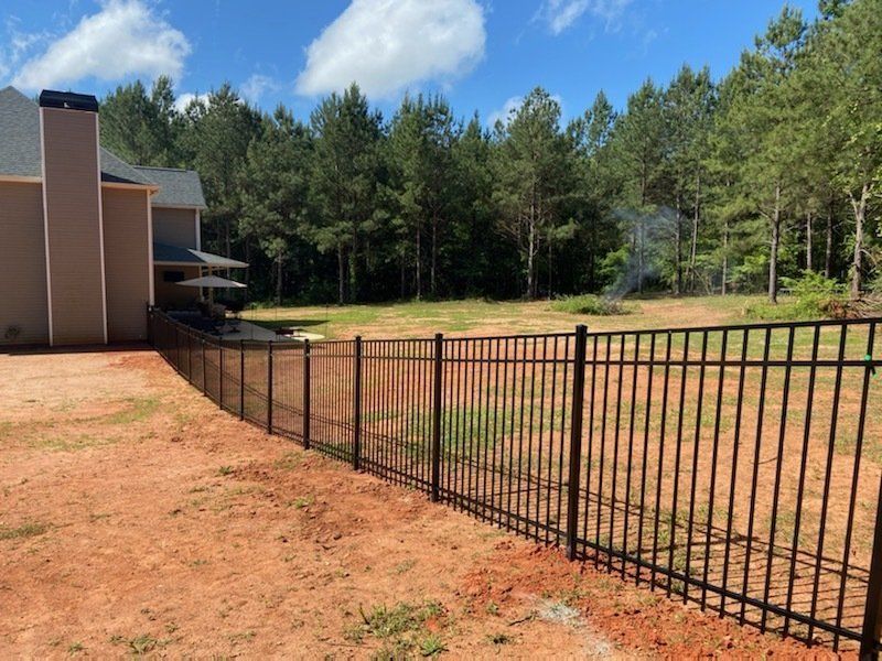 A black fence surrounds a lush green field in front of a house