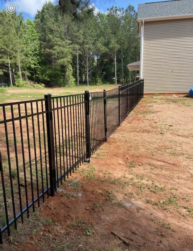 A black metal fence surrounds a dirt yard in front of a house.