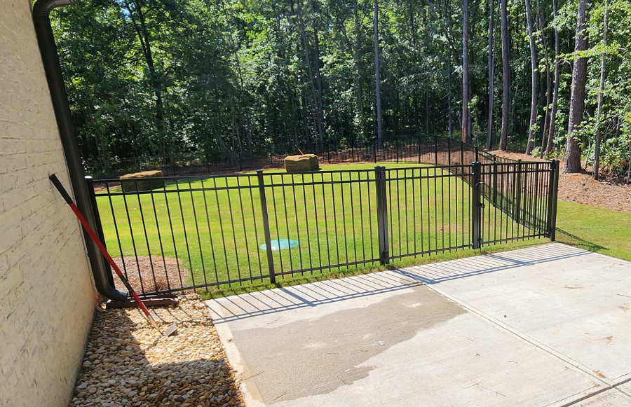 A fence surrounds a lush green yard with trees in the background.