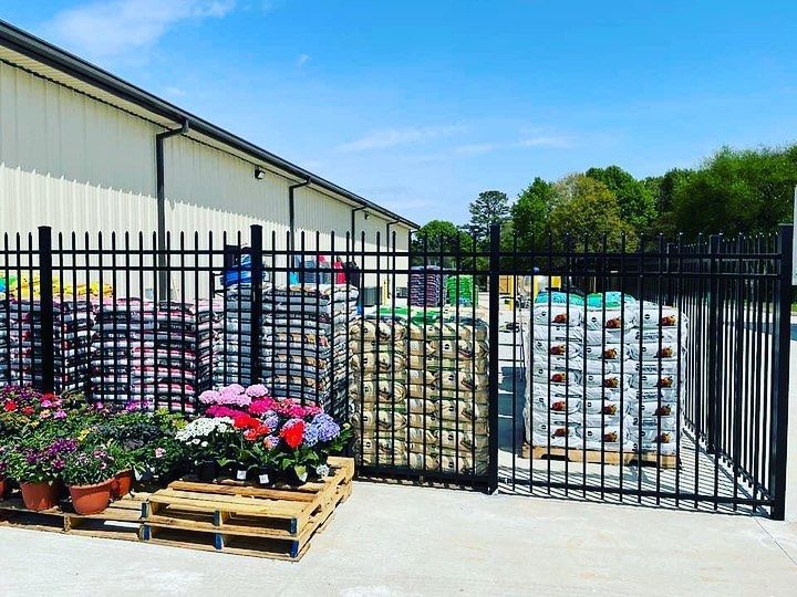 A fence with flowers on pallets in front of a building