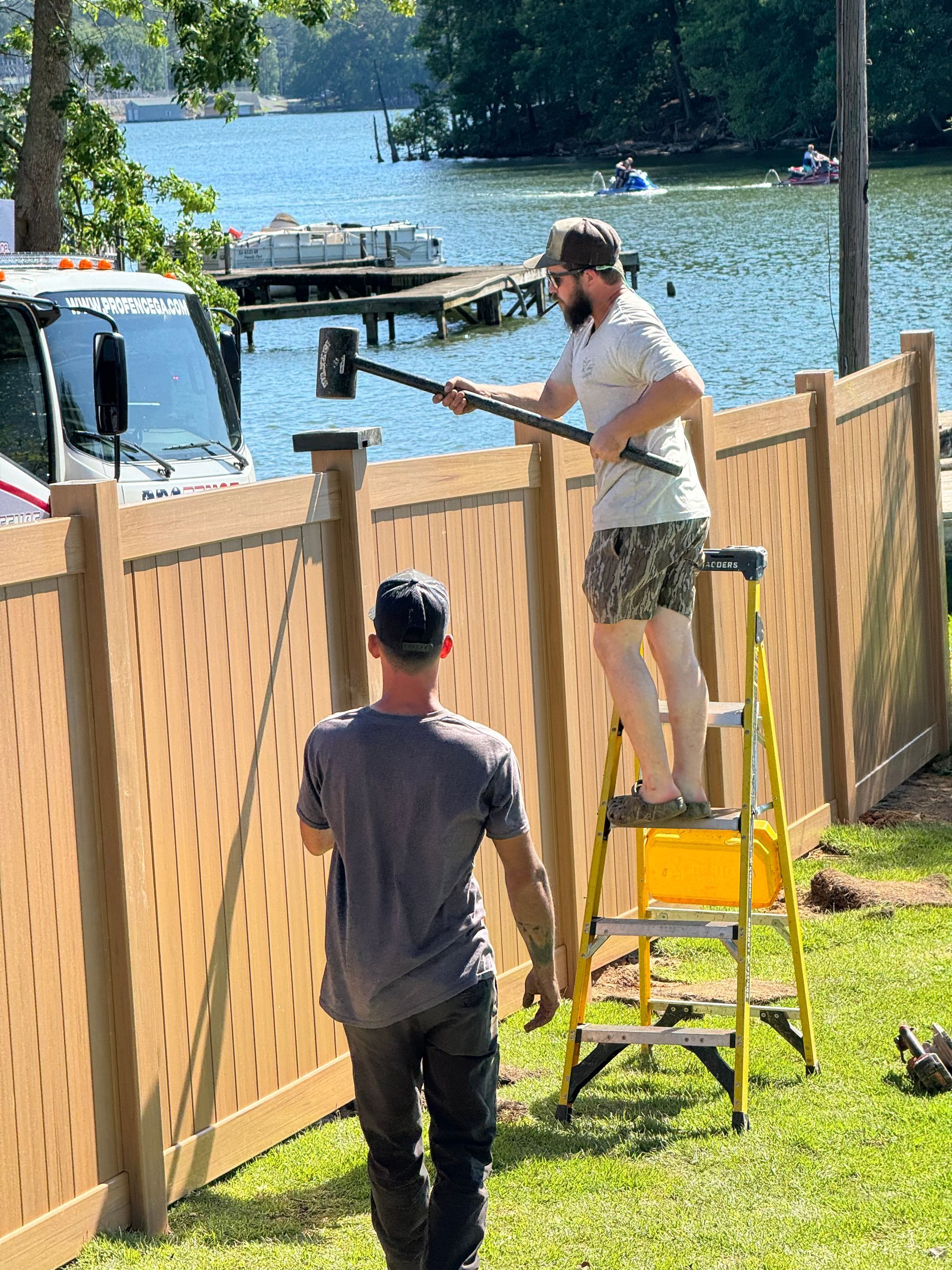 Two men are working on a wooden fence next to a body of water