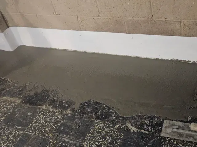 A person is laying concrete on the ground next to a brick wall.