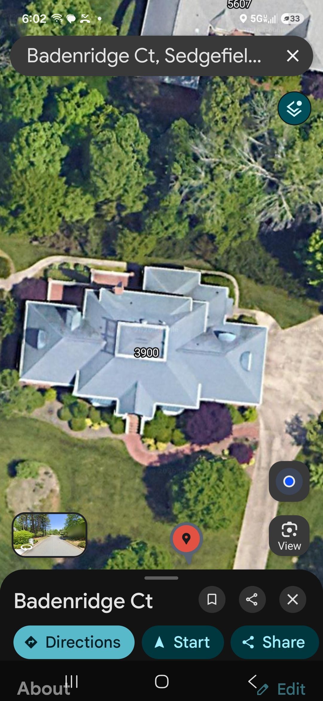 Satellite view of a gray-roofed house surrounded by trees, with map pins and location controls visible