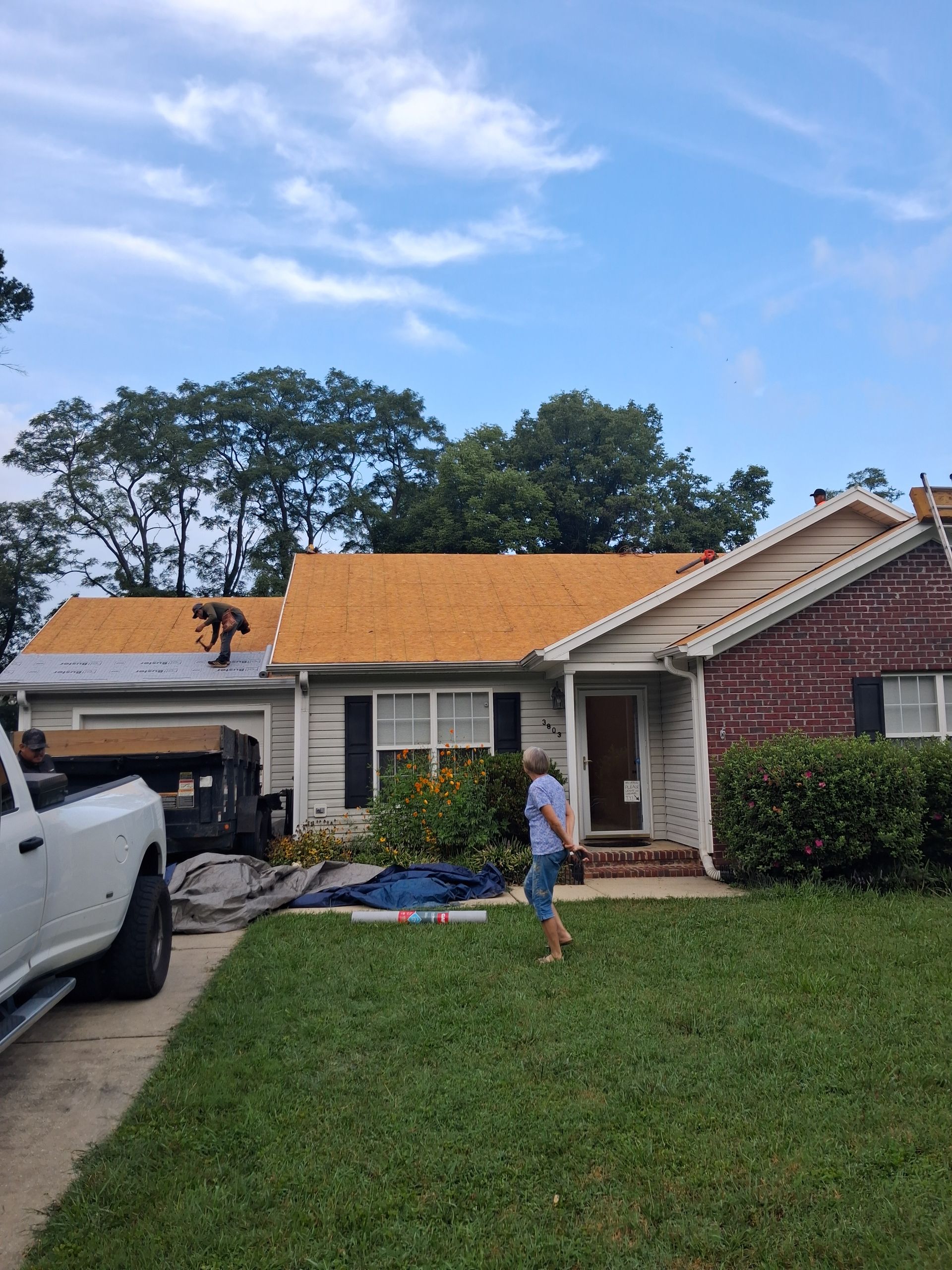 Residential house with orange roof tarp, a white truck in driveway, and a person standing on the lawn.