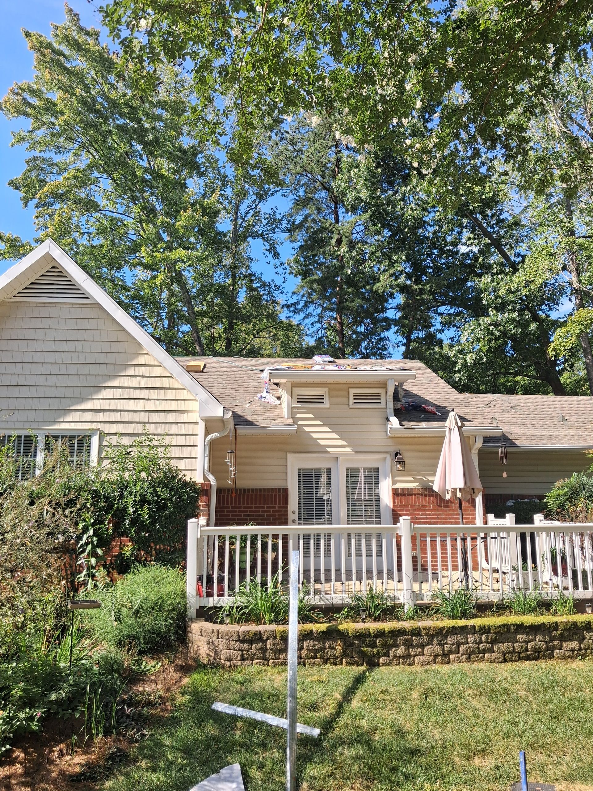 House with white porch railing and large trees in front yard on a sunny day