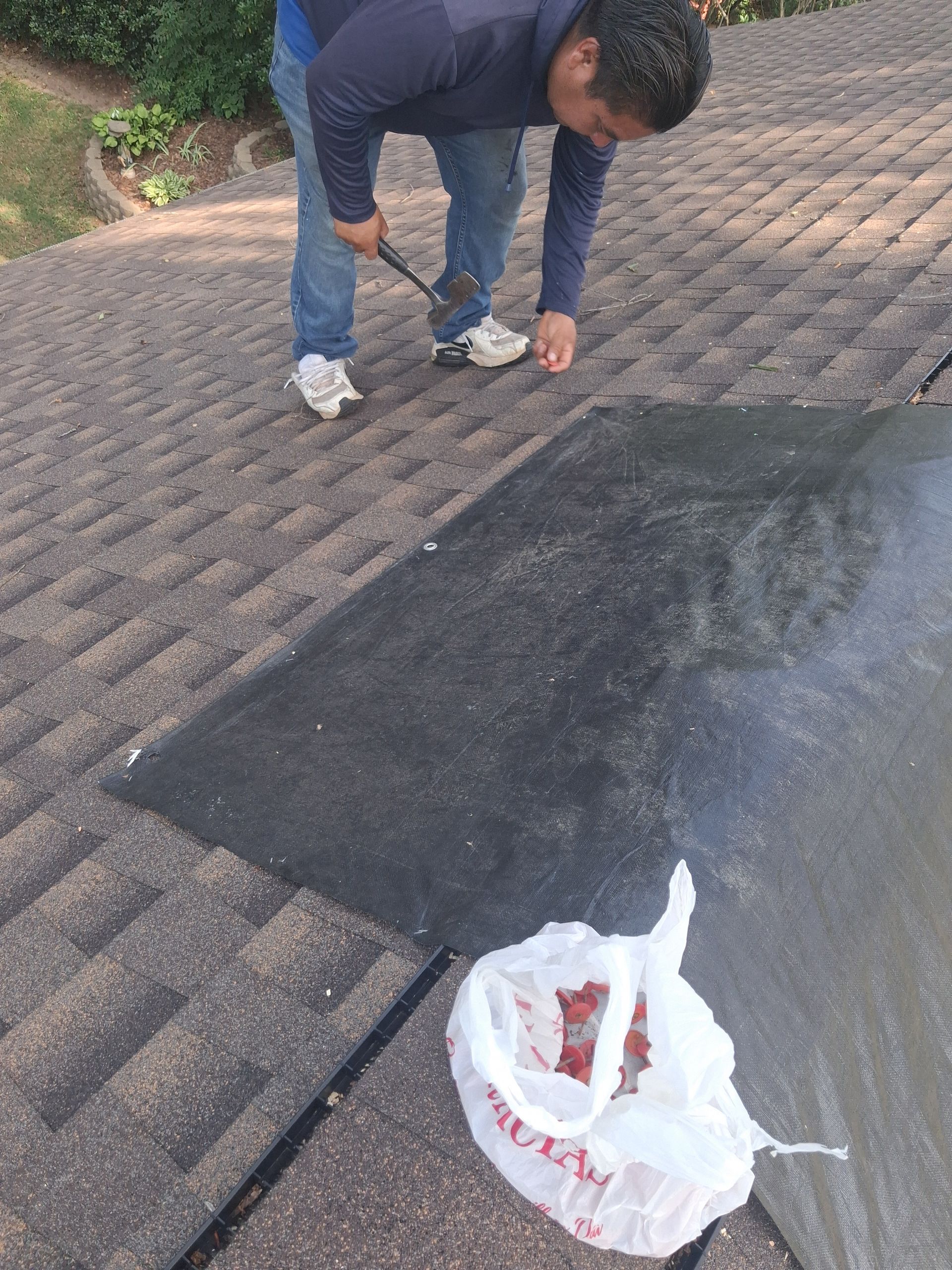Person bending over to pick up litter on a paved driveway beside a white plastic bag.