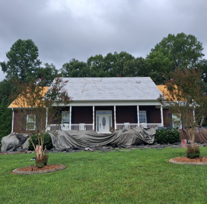 Front porch home with tarp-covered facade and damaged roof after storm, under cloudy skies