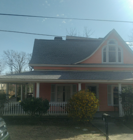 Pink house with white trim and porch in a sunny yard, seen from the front
