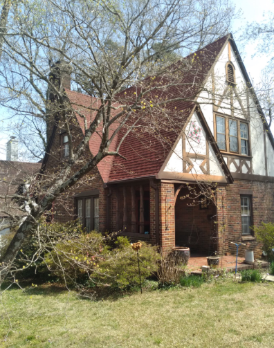 Brick and Tudor-style house with steep red roof and leafless trees in front yard