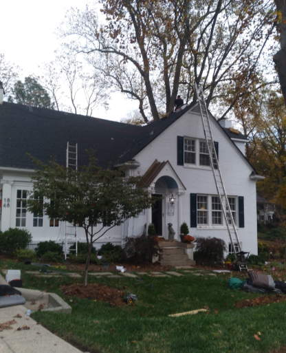 White house with black roof, front porch, and autumn trees in the yard.