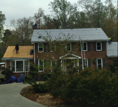 Brick house with workers replacing the roof and a black car in the driveway