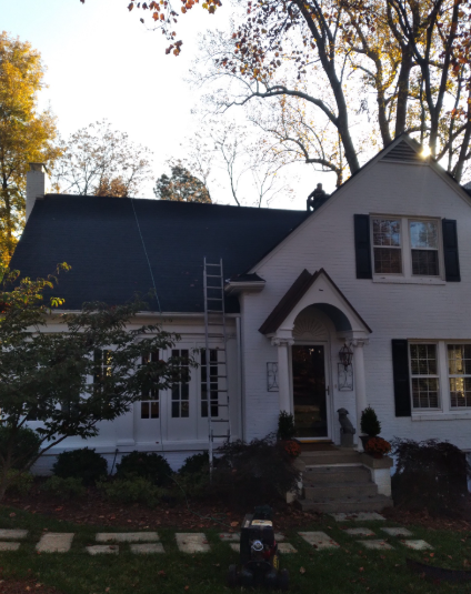 White house with dark roof and front porch, framed by autumn trees and a stone path.