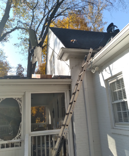 Ladder leaning against a white house roof beside a porch and window under autumn trees