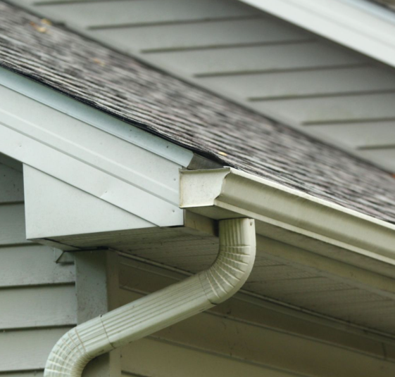 House roof eave with white gutter and downspout on gray siding