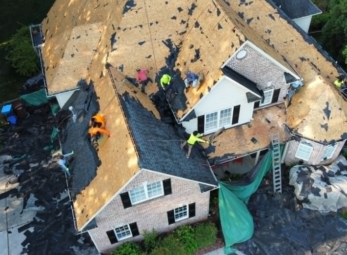 Aerial view of roof damage after a storm, with workers repairing the house and blue tarps below.