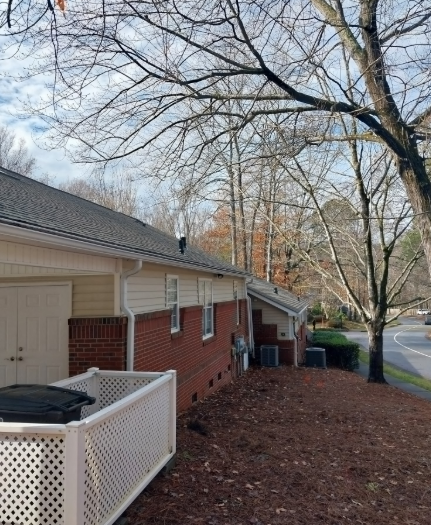 Brick townhouse beside a tree-lined street, with a white lattice fence and fallen leaves in the yard.