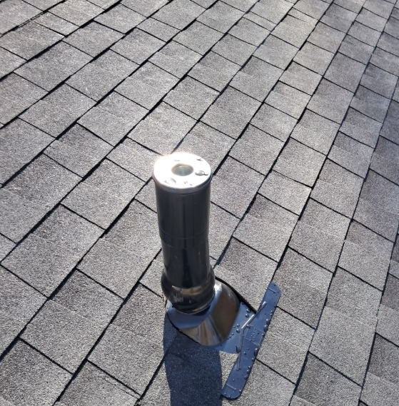 Black roof vent pipe on gray shingle roof with flashing under bright sunlight