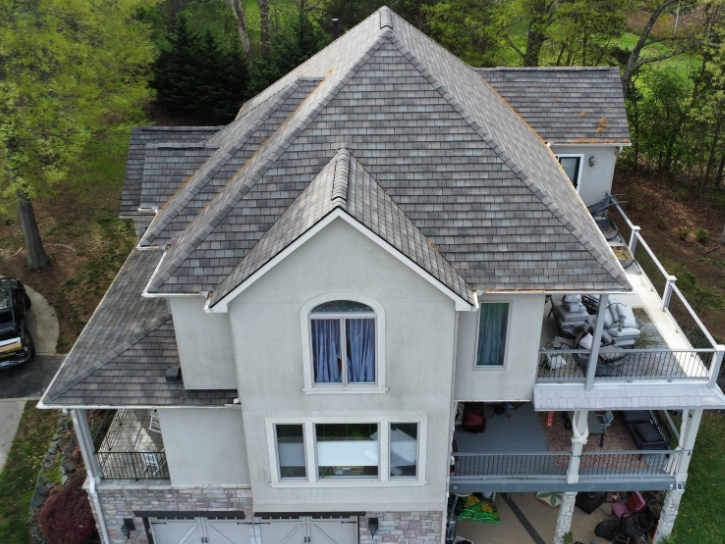 Aerial view of a gray house with a steep roof and white balconies surrounded by trees