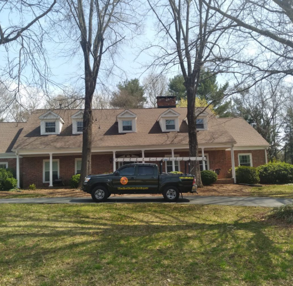 Brick house with dormer windows, front porch, and a black pickup truck parked in the driveway under bare trees