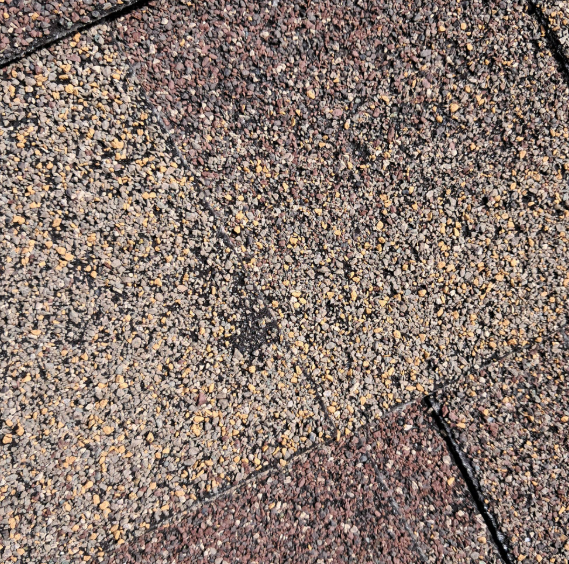Close-up of textured gray, tan, and maroon roofing shingles with a small crack