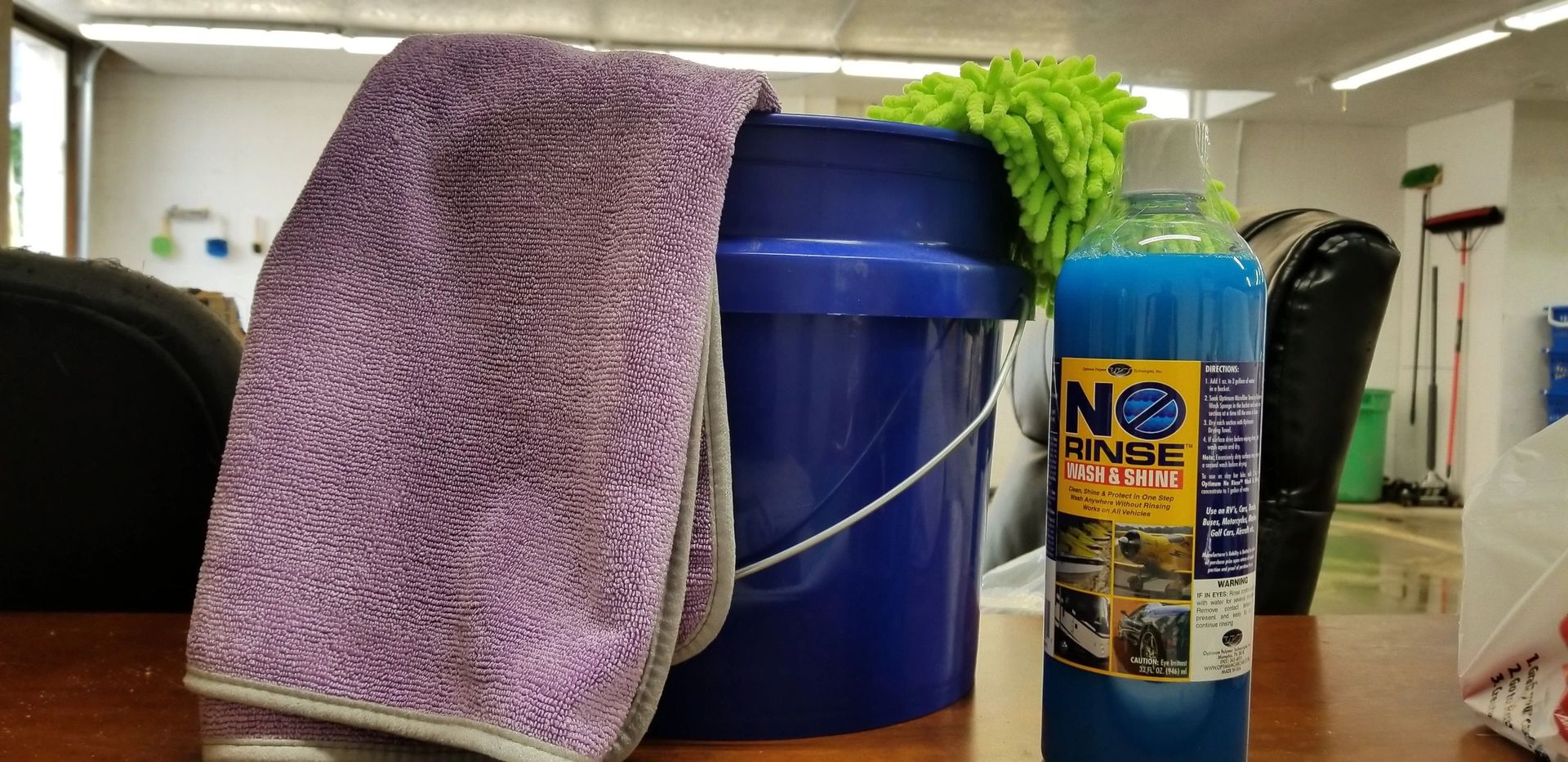 A purple towel is sitting next to a blue bucket and a bottle of no rinse water.