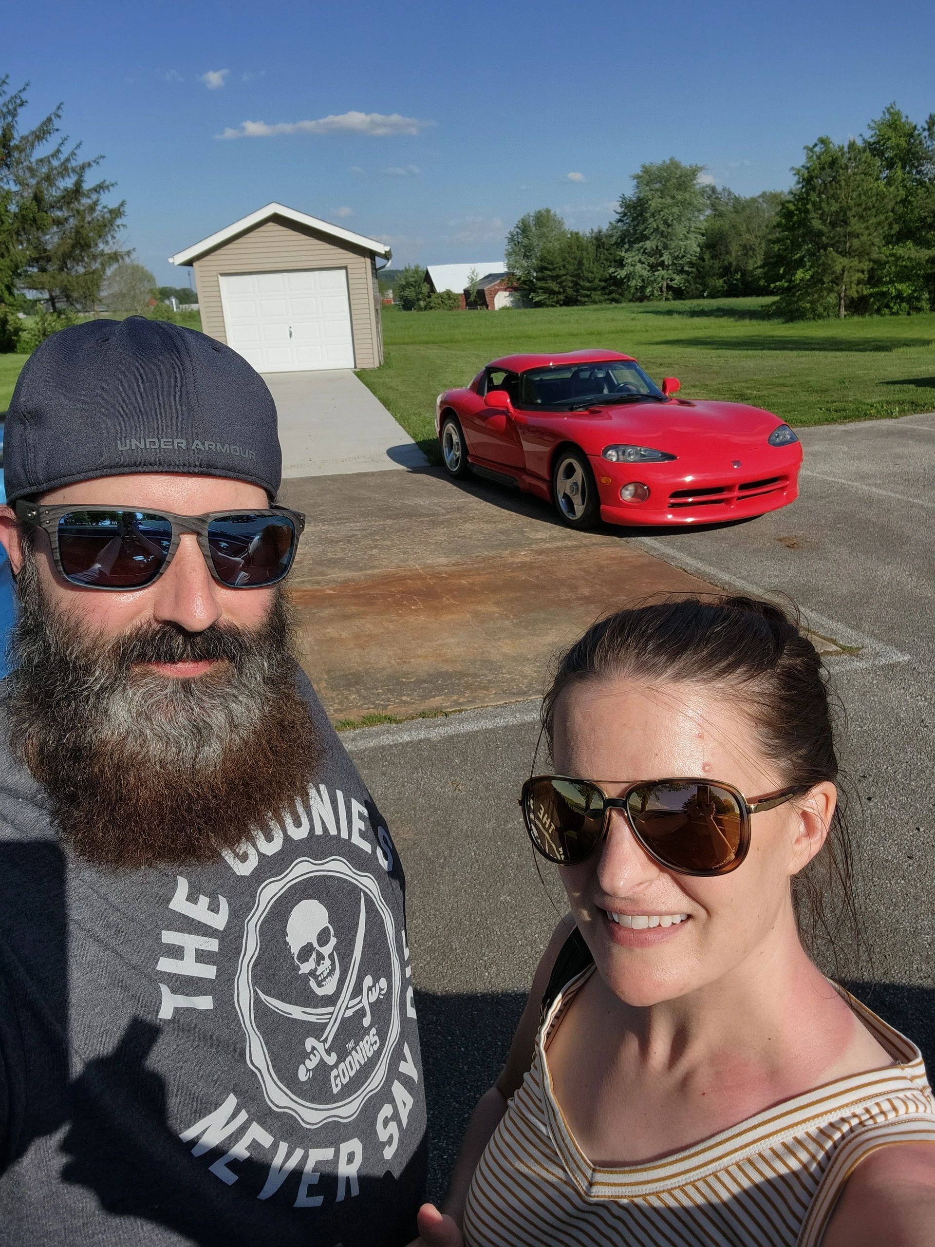 A man and a woman are posing for a picture in front of a red car.