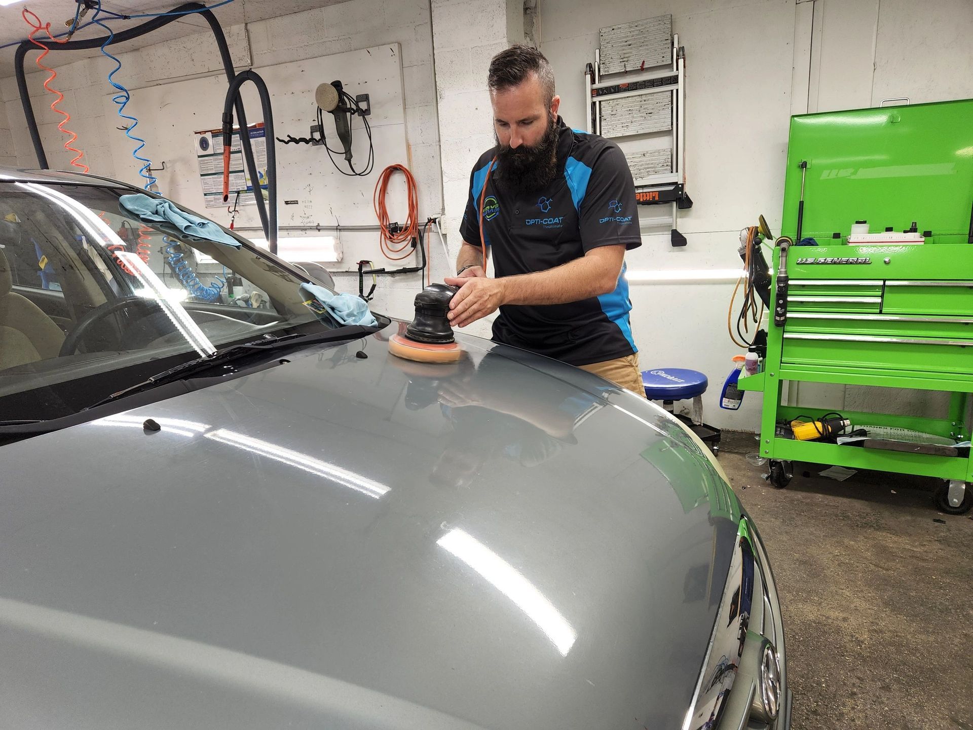 A man is polishing the hood of a car in a garage.