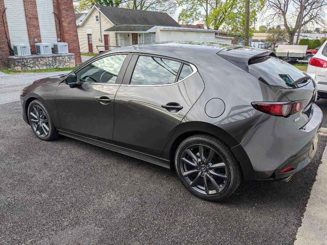 A black mazda 3 hatchback is parked in a parking lot.