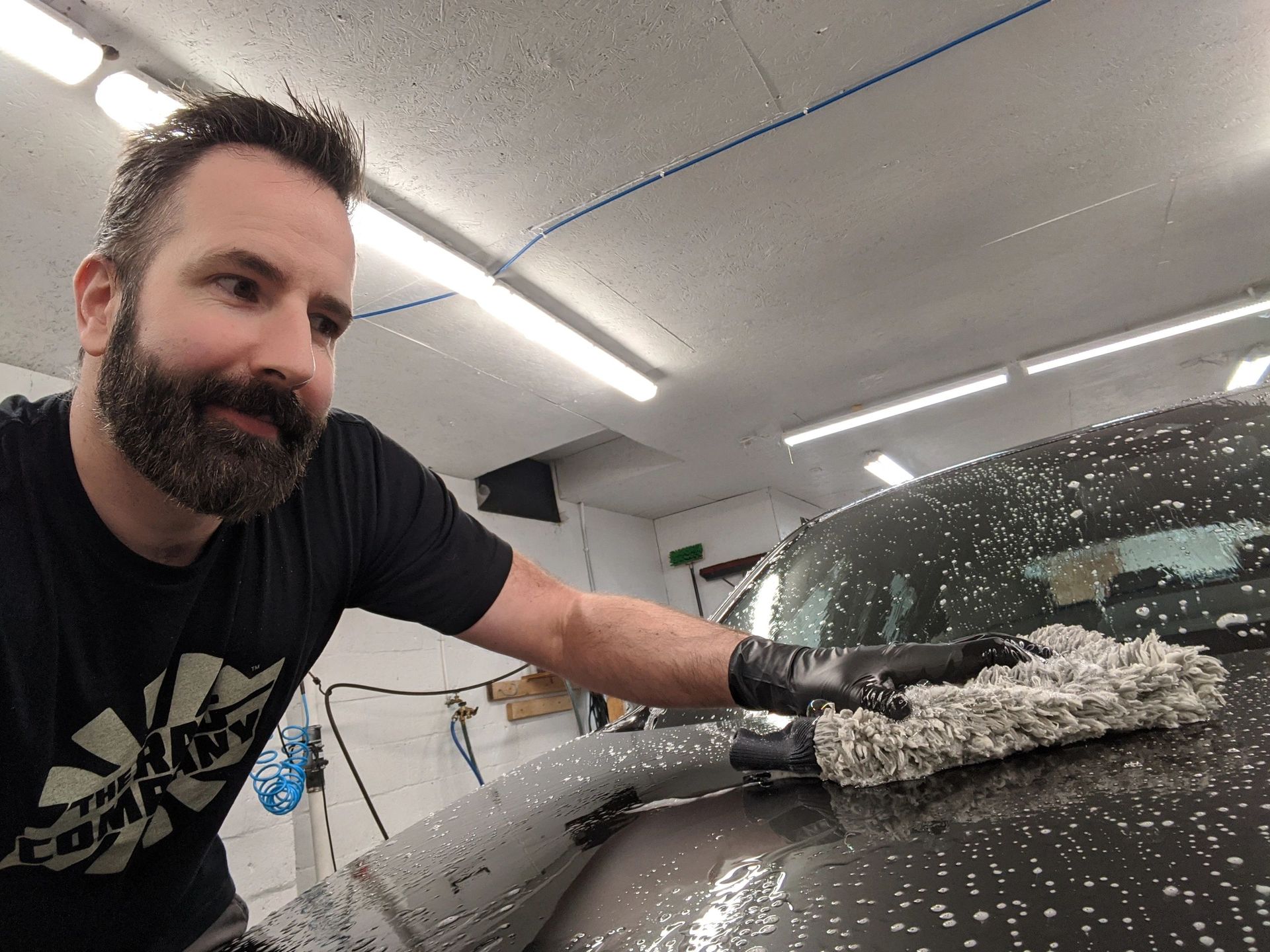 A man with a beard is washing a car in a garage.