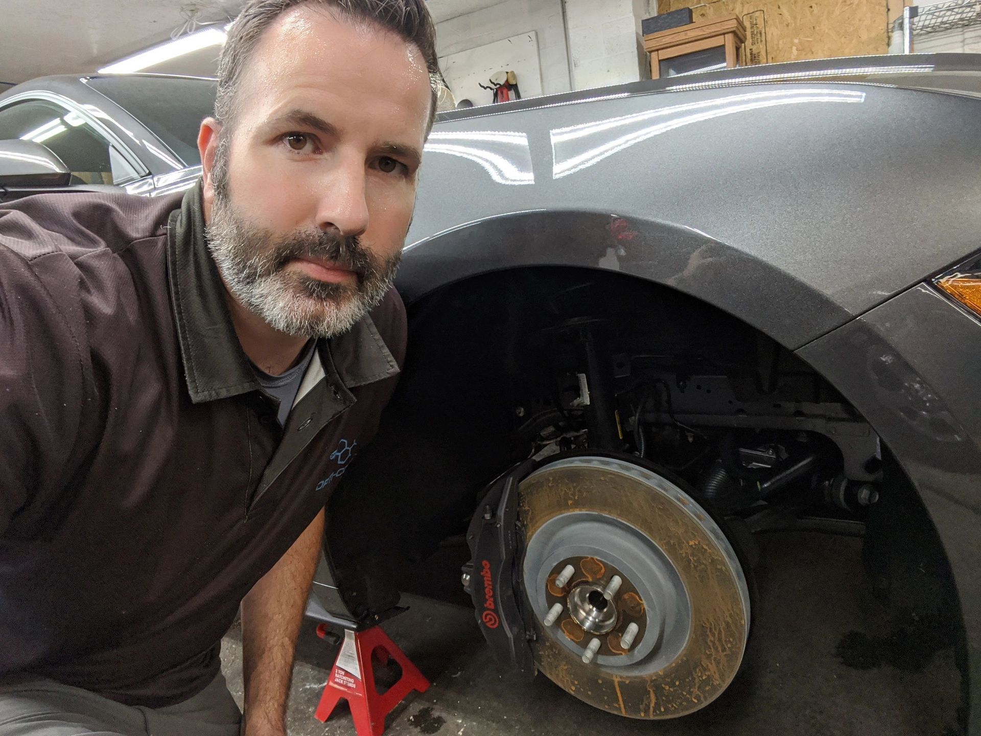 A man is kneeling down next to a car with a wheel on a jack.