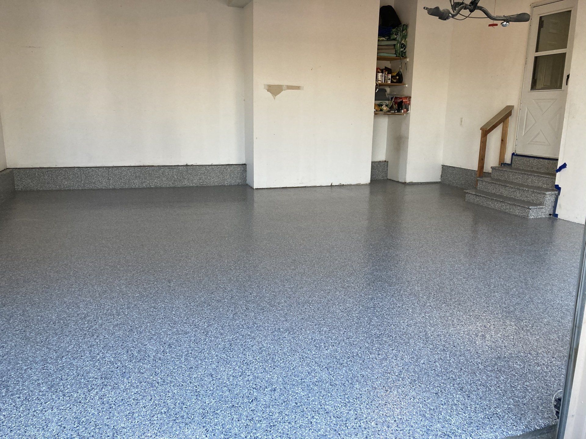 Garage with a shiny, speckled epoxy floor. White walls, steps leading up to a door.