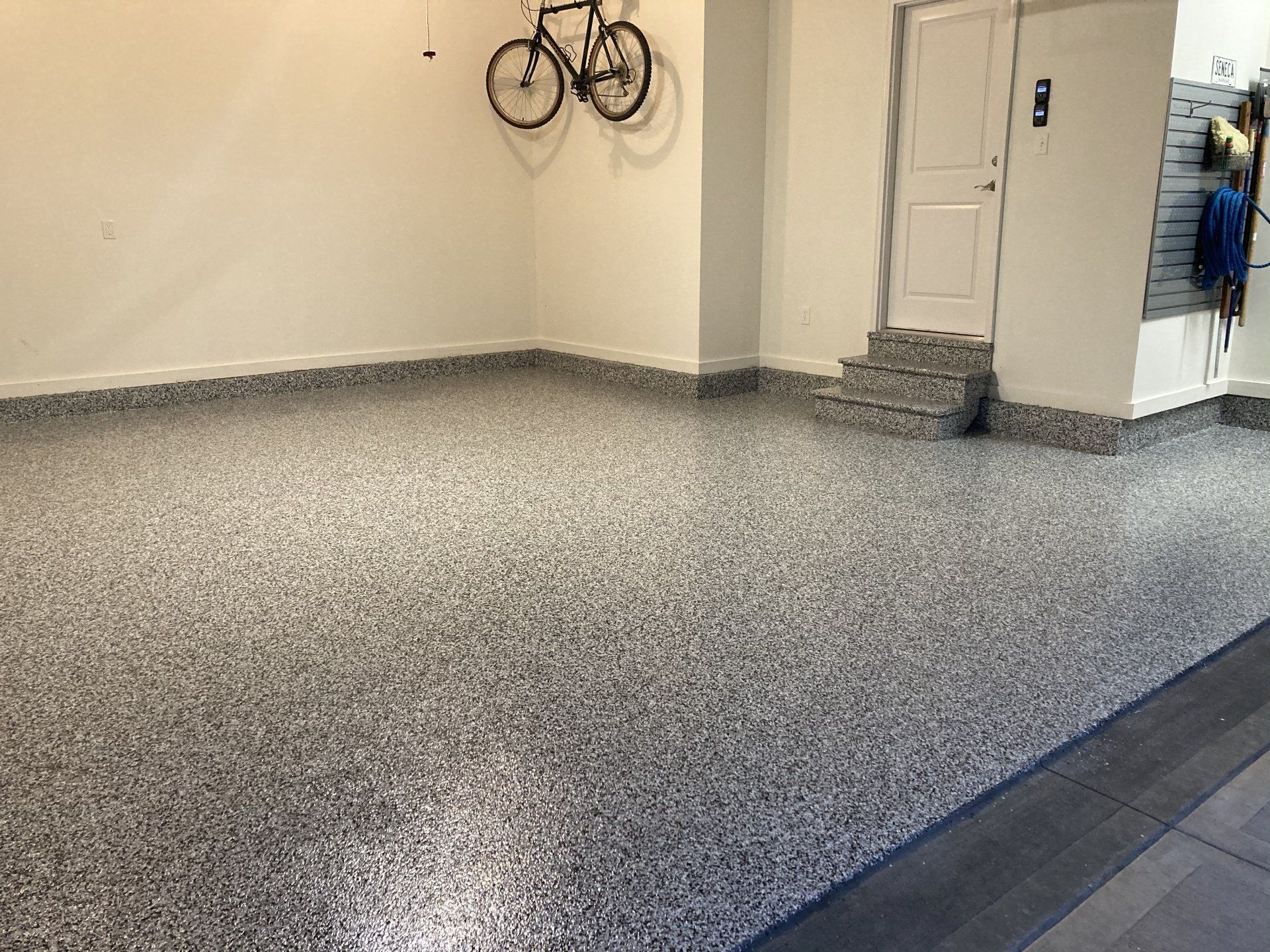 Garage with gray speckled epoxy flooring, white walls, bicycle, and door.