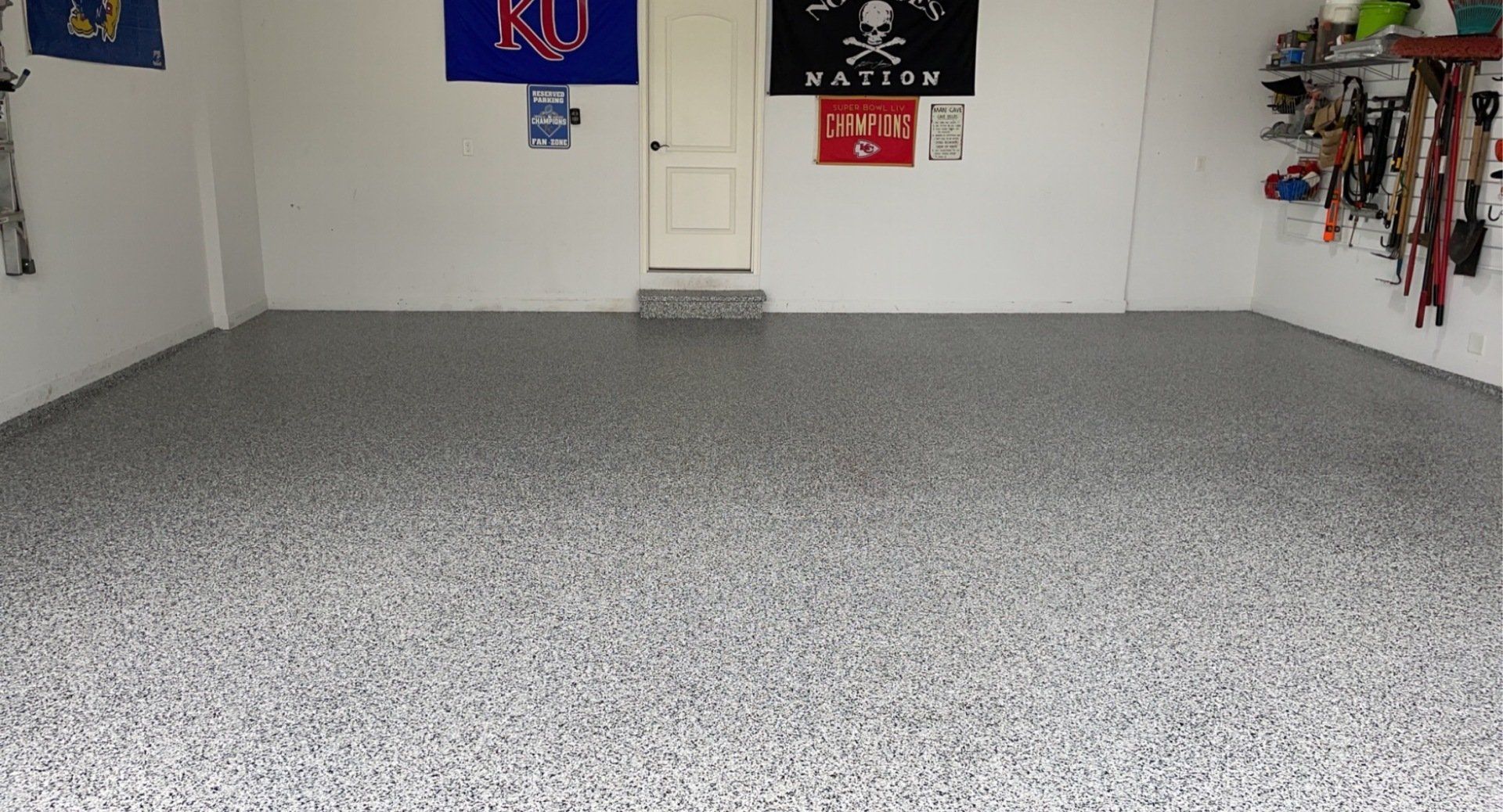 Garage with gray speckled epoxy floor and white walls. Flags and tools are visible.