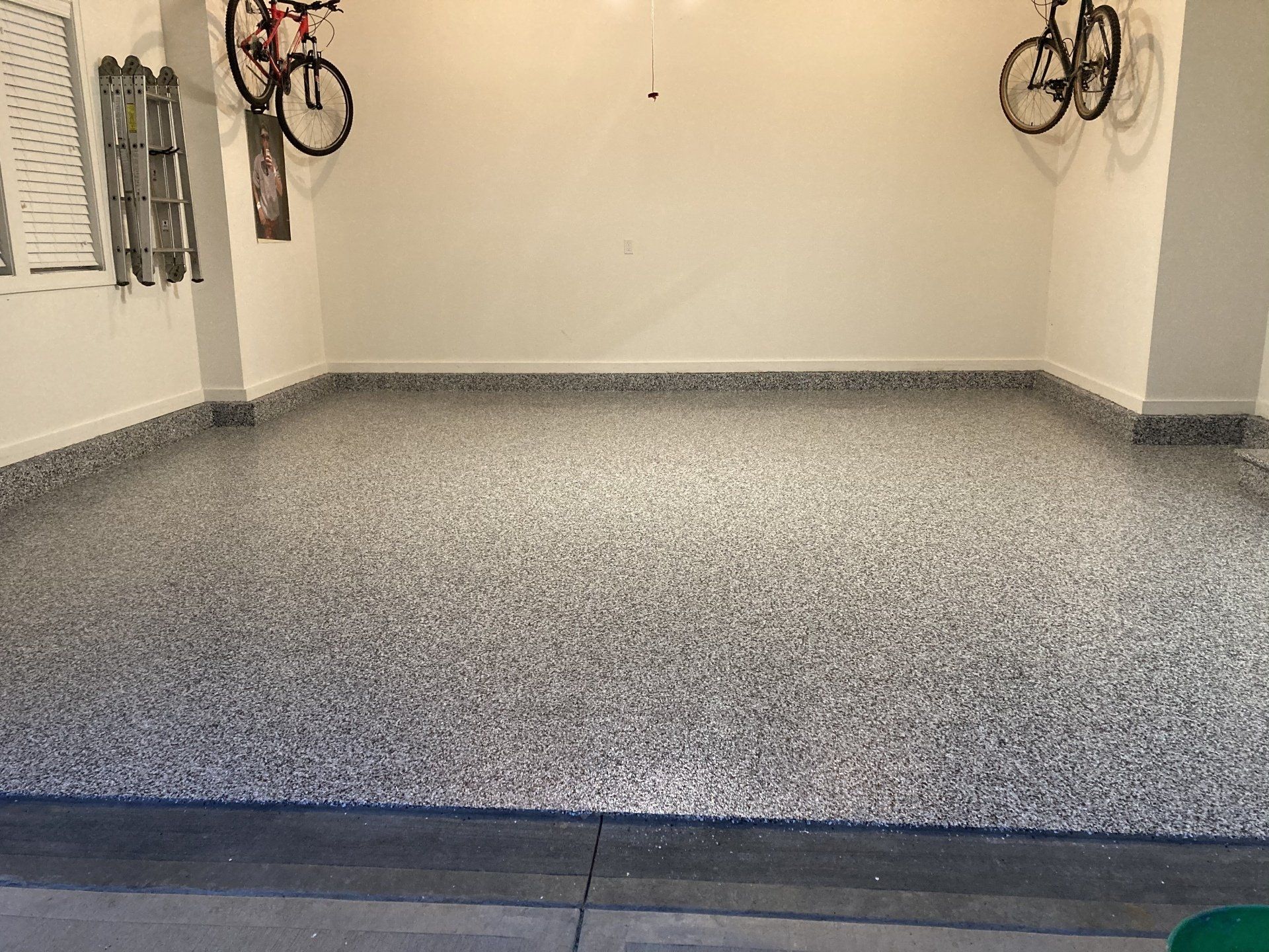 Garage with speckled epoxy floor, white walls, and two hanging bicycles.