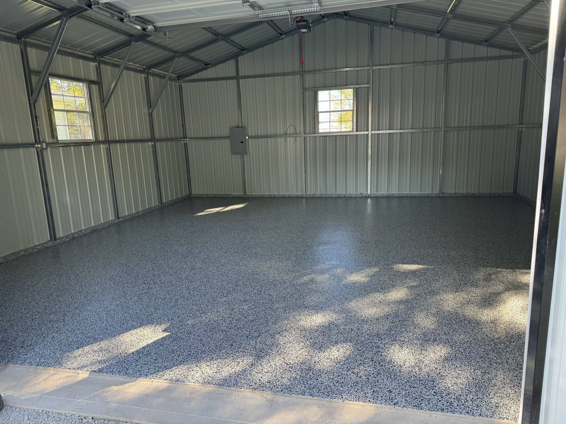 Interior of a metal shed with a speckled gray epoxy floor, two windows, and exposed metal framing.
