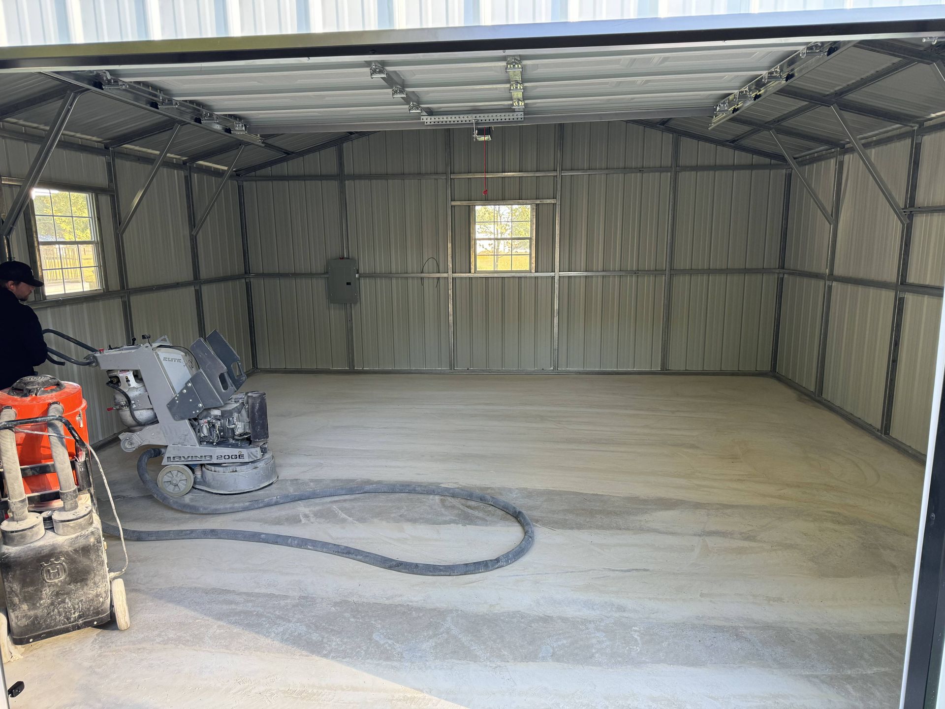 Man operating a concrete grinder in a metal building. The floor is light gray.
