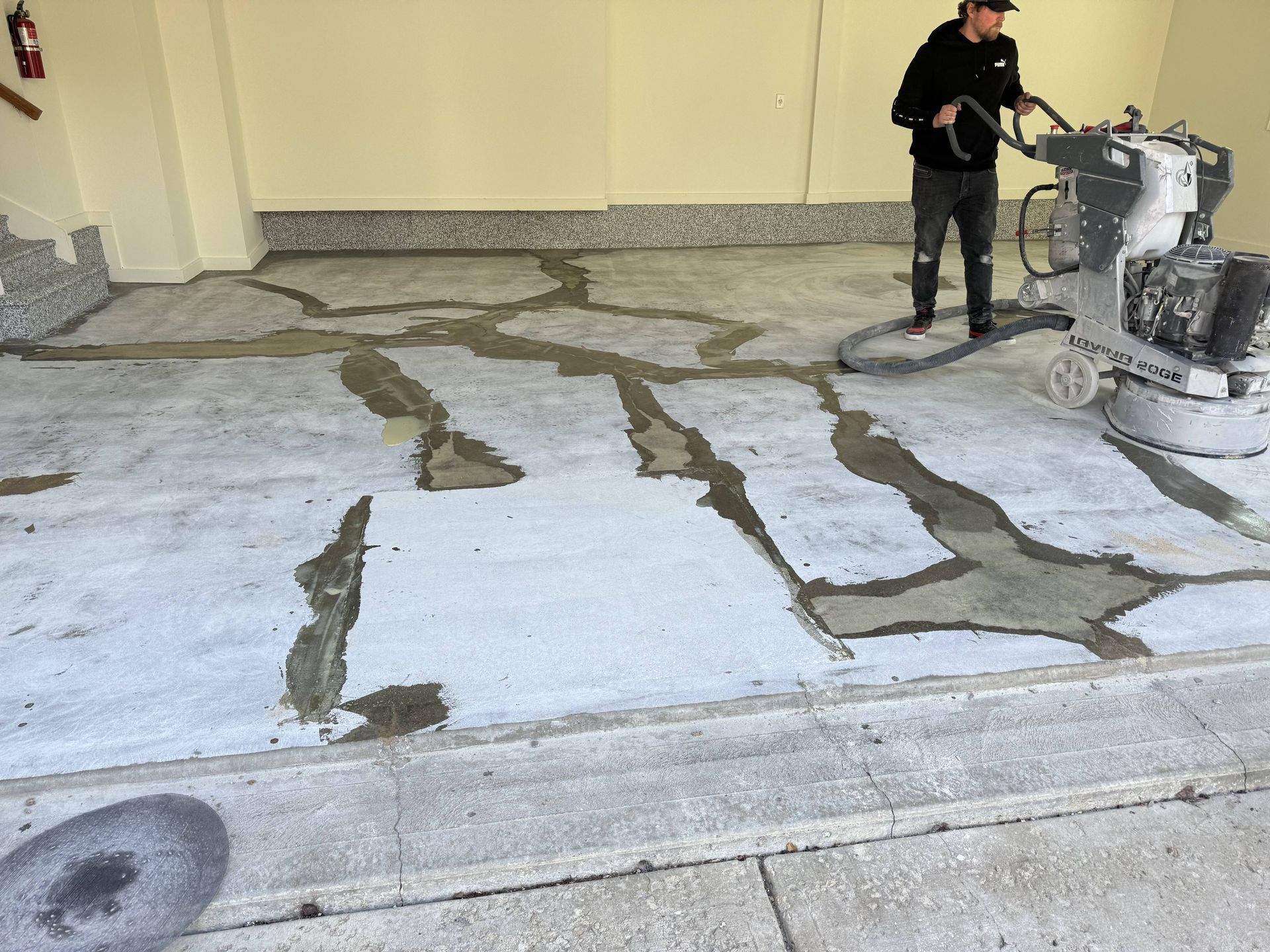 Man operating a concrete grinder inside a garage, grinding cracks in the concrete floor.