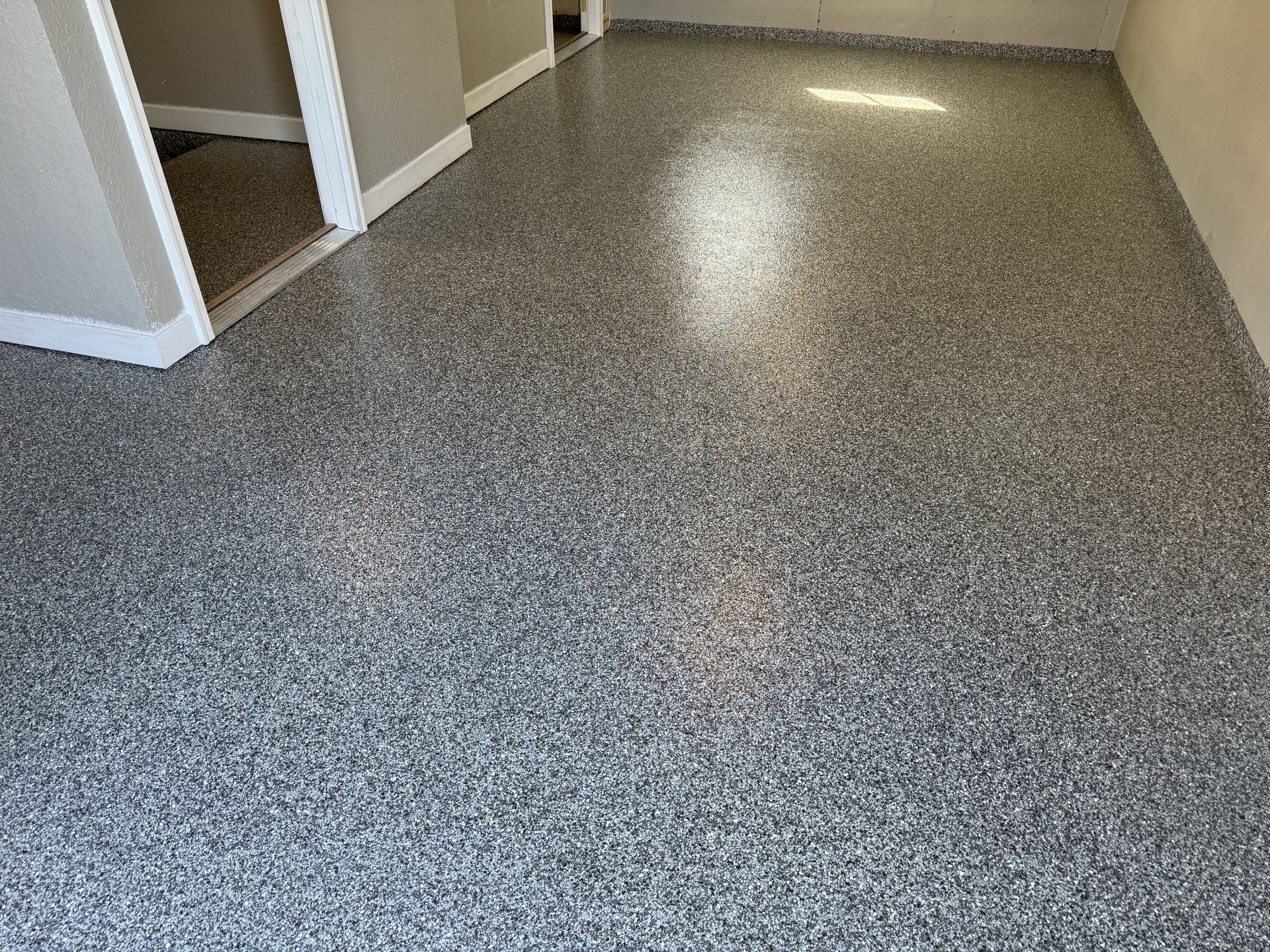 Epoxy-coated floor with speckled gray and black chips, next to a doorway and light-colored walls.